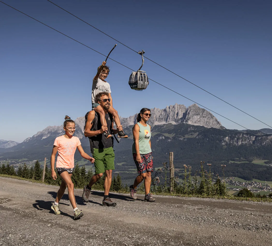 Familie wandert in St. Johann mit Seilbahn im Hintergrund.