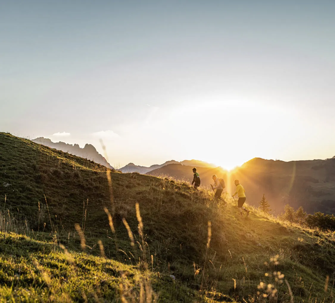Zwei Wanderer auf einer Wiese bei Sonnenuntergang, Berge im Hintergrund