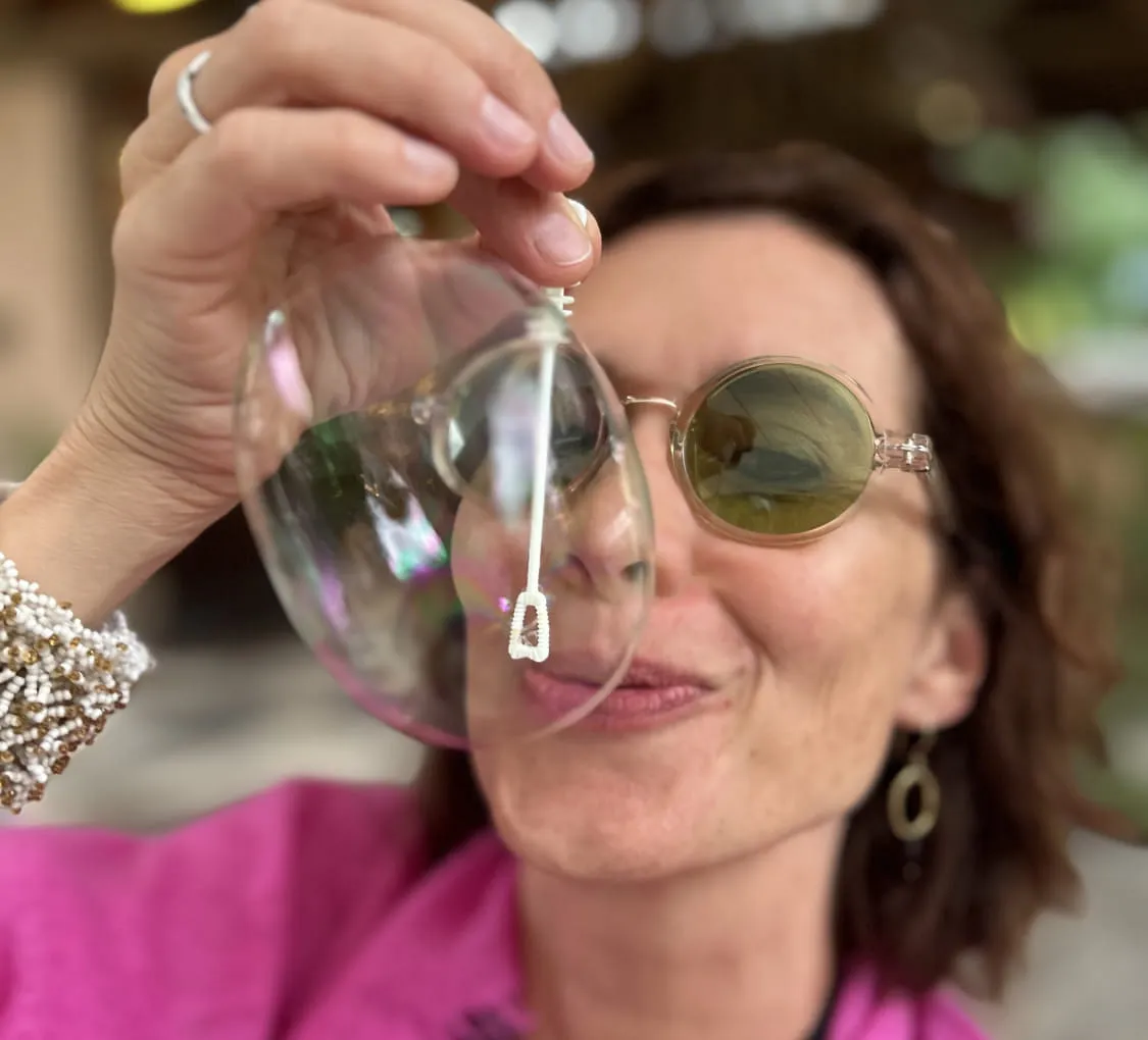 Frau mit Sonnenbrille hält ein Glas vor ihr Gesicht.