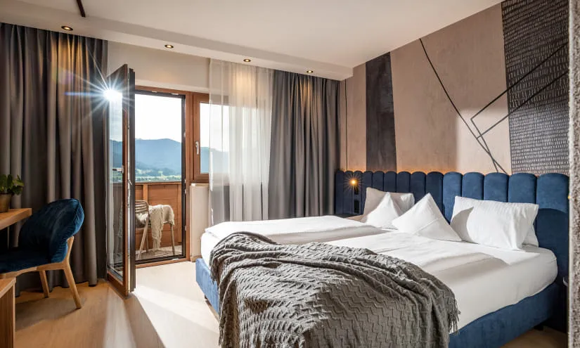 Helles Zimmer mit Doppelbetten und Balkonblick auf die Berge