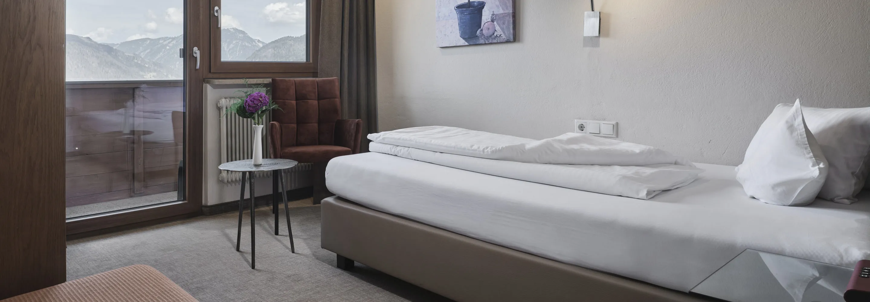 Helles Zimmer mit Balkon, Bett und gemütlichem Sessel.