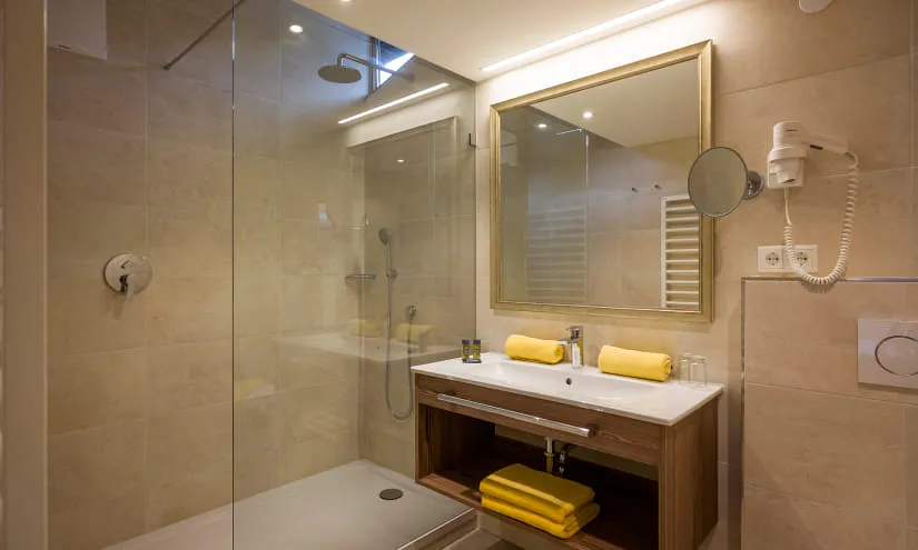 Modernes Badezimmer mit Dusche, Spiegel und gelben Handtüchern.