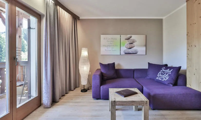 Wohnzimmer mit lila Sofa, Tisch und Lampen, Fenster zur Terrasse