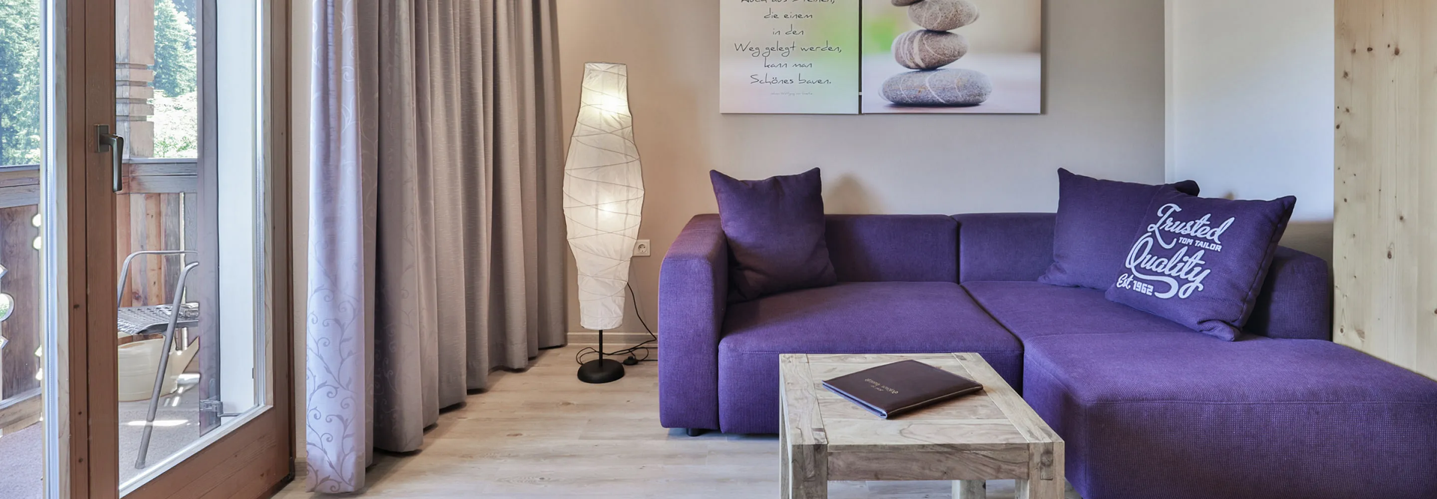 Wohnzimmer mit lila Sofa, Tisch und Vorhängen.