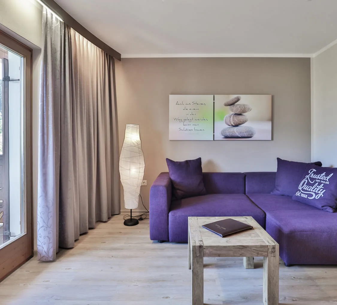 Wohnzimmer mit lila Couch und Holztisch, große Fenster